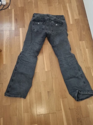 Svarta bootcut jeans - Säljer ett par svarta bootcut jeans med klassisk femficksdesign och knappgylf. Jeansen har en tvättad look och raka ben som går ut lite nedtill. Perfekta för dig som gillar en avslappnad och trendig stil.