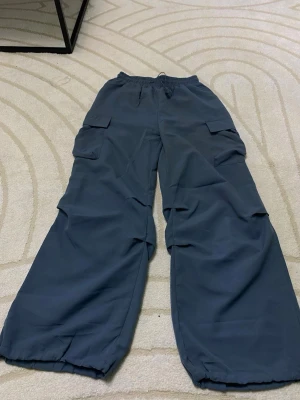 Mörkblå cargobyxor med dragsko - Säljer ett par mörkblå cargobyxor med bred passform och elastisk midja. Byxorna har stora fickor på sidorna och dragsko vid bensluten för en justerbar look. Perfekta för en avslappnad streetwear-stil.
