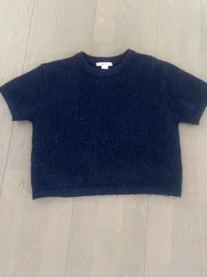 Mörkblå stickad t-shirt Gina Tricot - Kortärmad stickad t-shirt i mörkblått från Gina Tricot. Tröjan har rund halsringning och är gjord i ett mjukt, luddigt material som ger en mysig känsla. Perfekt för dig som vill ha en enkel men ändå trendig stickad topp.