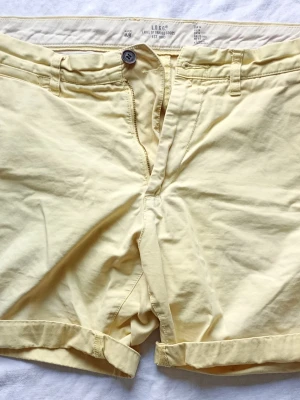 Ljusgula shorts från L.O.G.G. - Snygga ljusgula shorts från L.O.G.G. med upprullade benslut och klassisk knapp- och dragkedjestängning. Shortsen har bälteshällor och en enkel, stilren design som passar perfekt till sommaren.