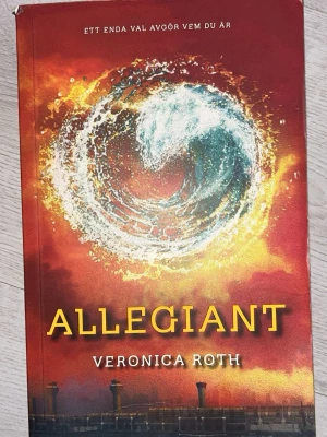 Allegiant av Veronica Roth - Säljer boken 'Allegiant' av Veronica Roth, sista delen i Divergent-trilogin. Omslaget är rött och orange med en stor vattenvirvel i centrum. Boken är på svenska och tryckt i pocketformat. Perfekt för dig som gillar dystopisk ungdomslitteratur.