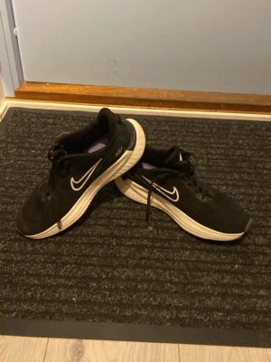Nike svartvita sneakers - Säljer ett par svarta Nike sneakers med vit sula och vit swoosh-logga på sidan. Skorna har mesh-överdel för bra ventilation och detaljer i turkos och svart vid hälen. Klassisk låg modell med snörning och bekväm dämpning i sulan. Tvättas innan frakt!