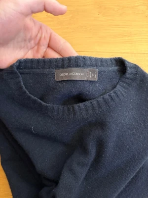 Mörkblå stickad tröja Oscar Jacobson - Klassisk mörkblå stickad tröja i merinoull från Oscar Jacobson. Den är i jättebra skick och sparsamt använd, dessutom inga tecken på användning.