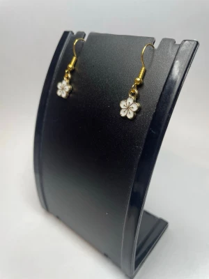 Blommiga vita örhängen med gulddetaljer - Söta örhängen med små vita blommor och guldfärgade krokar. Blommorna har fem kronblad och en diskret gulddetalj i mitten. Perfekta för dig som gillar en feminin och lekfull stil.