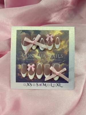 DollCore (M);Medium Almond - Snygga handgjorda press-on naglar i en medium almondform med fransk manikyr-look. Naglarna är nude med vita tippar och dekorerade med söta rosa rosetter i M: 16 mm, 12 mm, 12,5 mm, 11,5 mm, 10 mm. Perfekt för dig som vill ha en gullig och trendig nagelstil.