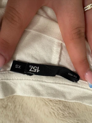 Vit ärmlös t-shirt från 157 - Säljer en enkel och stilren vit t-shirt från 157 i storlek XS. Modellen är ärmlös med rund halsringning och tillverkad i mjukt bomullsmaterial. Perfekt för dig som gillar minimalistisk och clean stil.