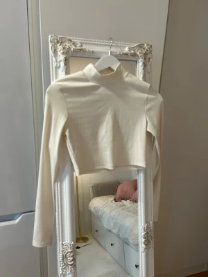 Vit croppad polotopp från Ivyrevel - Säljer en stilren vit croppad polotopp från Ivyrevel. Toppen är ribbad, har lång ärm och hög krage som ger en trendig look. Perfekt att matcha med höga jeans eller kjol. Materialet är mjukt och stretchigt, vilket gör den bekväm att bära.