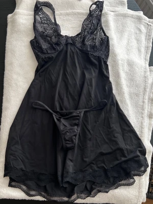 Svart spetsbody med stringtrosa - Ny pris 399kr. Snyggt set med svart body och matchande stringtrosa. Bodyn har spetsdetaljer upptill, justerbara axelband och vacker spetskant nedtill. Materialet är mjukt och följsamt, perfekt för en elegant look. Inget synligt märke. Provat och en pearl detalj saknas i mitten av kuporna! Mycket sköna babydoll