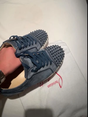 Christian Louboutin  - Snygga blåa sneakers från Christian Louboutin i mocka med coola nitar på tån och matchande blå skosnören. Skorna är i storlek 41 men passar mig som har 42. Skorna har en blod röd sula och den klassiska Louboutin-looken.  Perfekta för dig som vill sticka ut med stilrena detaljer. Dessa skor är självklart äkta skriv vid minsta lilla fundering!!🤝