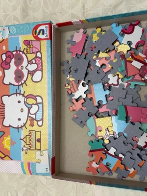 Hello Kitty pussel från Schmidt - Säljer ett färgglatt Hello Kitty pussel från Schmidt med motiv av Hello Kitty på stranden. Pusselbitarna är av kartong och har olika färger som rosa, blå, gul och vit. Perfekt för dig som gillar söta och lekfulla motiv.