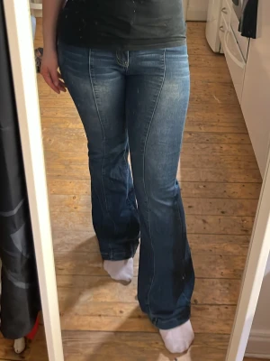 Blå bootcut jeans med hög midja - Säljer ett par blå bootcut jeans med hög midja och klassiska fickor både fram och bak. Jeansen har en snygg tvätt och markerade sömmar som ger en retrovibe. Perfekta för dig som gillar en avslappnad men ändå trendig stil.