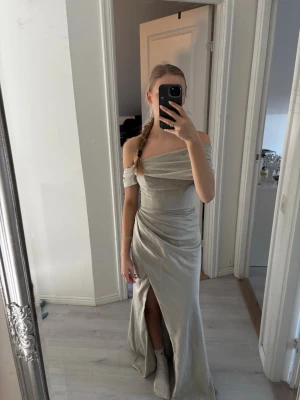 Ljusgrön balklänning - Elegant ljusgrön balklänning med offshoulder-design och draperad överdel. Klänningen har en hög slits framtill och smickrande omlott-detalj i midjan. Perfekt för bal eller festliga tillfällen.