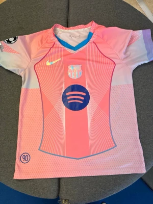 Barcelona rosa matchtröja Nike - Snygg Barcelona matchtröja i rosa och ljuslila med blå detaljer. Tröjan har tryck med Spotify-logga, klubbmärke och Champions League-märke på ärmen. På ryggen står det Lamine Yamal och nummer 10. Tillverkad i lätt och ventilerande material, perfekt för fotboll.