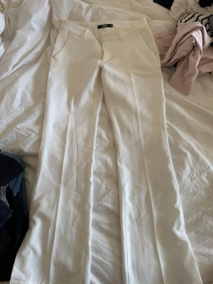 Vita kostymbyxor från Bik Bok - Snygga vita kostymbyxor från Bik Bok med raka/bootcut ben och pressveck. Byxorna har fickor i sidorna och hällor för skärp. Perfekta för en clean och stilren look. Materialet känns mjukt och har en lätt stretch för extra komfort.
