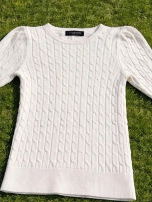 Vit kabelstickad tröja från Ralph Lauren - Kabelstickad vit tröja från Ralph  Lauren med rund halsringning och långa ärmar. Tröjan har puffade axlar och ribbade muddar vid ärmslut och nederkant. Perfekt för dig som gillar klassisk och stilren design.