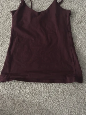 Mörklila linnetopp med smala band - Säljer en enkel och stilren mörklila linnetopp med smala axelband och v-ringad hals. Perfekt att matcha med jeans eller kjol för en clean look. Tyget känns mjukt och följsamt.