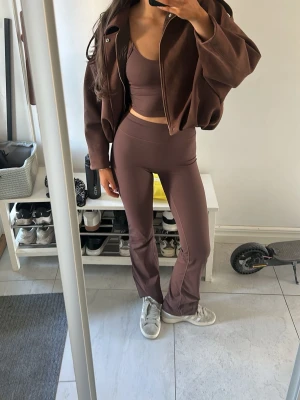 Brunt loungewear set med crop top - Säljer ett brunt loungewear set med croppad topp och matchande höga byxor med utsvängda ben. Materialet är mjukt och stretchigt, perfekt för chill dagar hemma. Jackan är oversized och har dragkedja framtill. Snygg och avslappnad look!