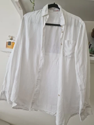 Vit linneskjorta med knappar - Klassisk vit skjorta i linne med lång ärm och bröstficka. Skjortan har en avslappnad passform och stängs med knappar framtill. Perfekt för en stilren och luftig look. Storlek 3, vet inte om det är herr eller dam skjorta. Carly Gry märke. 