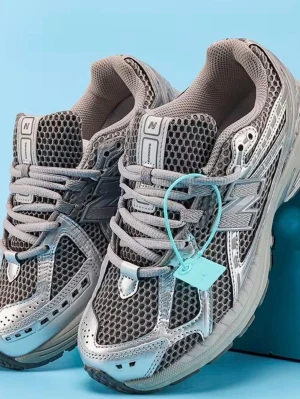 Grå New Balance sneakers med mesh - Grå sneakers från New Balance med ventilerande mesh och silvriga detaljer. Skorna har snörning, chunky sula och reflekterande partier. Perfekt för dig som gillar sportig och modern stil. Materialet är en mix av textil och syntet.