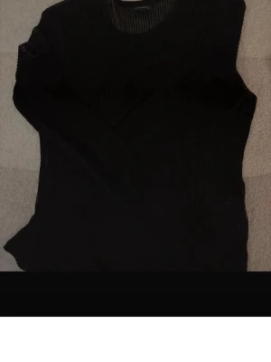 Svart ribbad tröja från Studio - Svart långärmad tröja från Studio i ribbat material. Tröjan har rund halsringning och en tight passform som passar perfekt till jeans eller kjol. Enkel och stilren design som funkar till många olika looks.