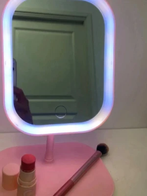 Rosa sminkspegel med LED-belysning - Snygg sminkspegel i rosa med inbyggd LED-belysning runt spegeln. Spegeln har en rektangulär form och står på en matchande rosa fot. Perfekt för att fixa sminket med bra ljus. Touchknapp på spegeln för att tända och släcka belysningen.Vikbar så man kan ta med sig överallt. 19x23