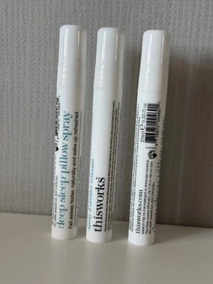 This Works Deep Sleep Pillow Spray - Tre vita sprayflaskor från This Works med texten 'deep sleep pillow spray'. Varje flaska innehåller 10 ml och är designad för att sprayas på kudden för en avslappnande och lugnande effekt. Enkel och smidig att ta med sig, perfekt för dig som vill ha bättre sömn.