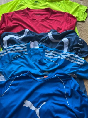 Färgglada sportiga t-shirts från Puma & Adidas - Säljer ett gäng sportiga t-shirts i olika färger från Puma, Adidas och andra varumärken shirtsen är kortärmade och finns i blått, rött och neongult. Perfekta för träning och har snygga loggor och detaljer. Olika storlekar 