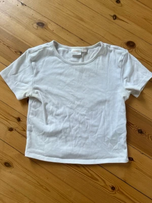 Vit basic t-shirt från Gina Tricot - En klassisk vit t-shirt från Gina Tricot i mjuk bomull. Modellen är kortärmad med rund halsringning och har en enkel, clean design som passar till allt. Perfekt för en stilren och avslappnad look.