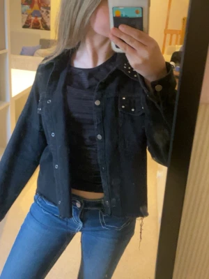 Intressekoll!! - Snygg svart jeansjacka med silverfärgade nitar på bröstfickorna och axlarna. Klassisk knappstängning framtill och två bröstfickor med lock. Jackan har en rak passform och är tillverkad i jeansmaterial. Perfekt för en cool och avslappnad stil.