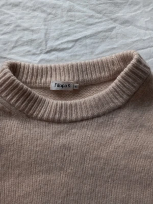 Beige stickad tröja från Filippa K - Säljer en beige stickad tröja från Filippa K med rund halsringning och ribbade muddar. Tröjan har en enkel och stilren design, perfekt att matcha med jeans eller kjol. Materialet känns mjukt och skönt mot huden. Den är lite kort i längden och använd bara några få gånger. Pris kan diskuteras.