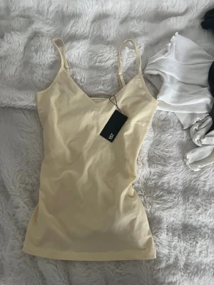 Gul linnetopp från lager 157 - Helt ny, Snygg gul linnetopp från lager 157 med smala axelband och v-ringad hals. Toppen är i ett mjukt bomullsmaterial och har en enkel, stilren design som passar perfekt till jeans eller kjol.
