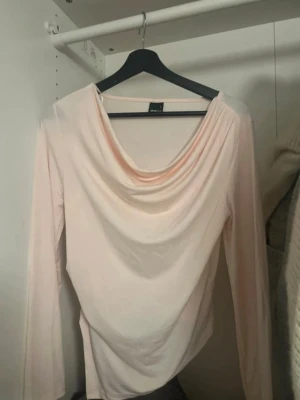 Ljusrosa långärmad topp med drapering - Säljer en ljusrosa långärmad topp med snygg draperad urringning. Toppen har en mjuk och följsam passform och är tillverkad i ett tunt, stretchigt material som känns skönt mot huden. Perfekt att styla med jeans eller kjol. Aldrig kommit till användning.