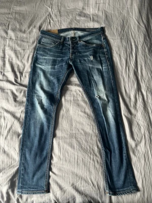 Dondup jeans - Storlek 30x32. Snygga blå slim fit jeans med slitningar och ljusa tvättade partier. Klassisk femficksmodell med dragkedjegylf och kontrastsömmar. Perfekta för en avslappnad och trendig look. 