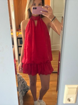 Röd halterneck klänning omlott - Säljer en röd halterneck klänning med omlott-design och öppen rygg. Klänningen har en lös passform, kort volangkjol och knyt i nacken. Perfekt för dig som vill sticka ut med en färgstark och unik look.