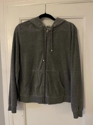 Grå zip hoodie med huva - En enkel och stilren grå hoodie med dragkedja framtill och två fickor. Hoodien har en justerbar huva med snören och ribbade muddar vid ärmar och nederkant. Perfekt för en avslappnad look och passar till det mesta. Materialet känns mjukt och bekvämt.