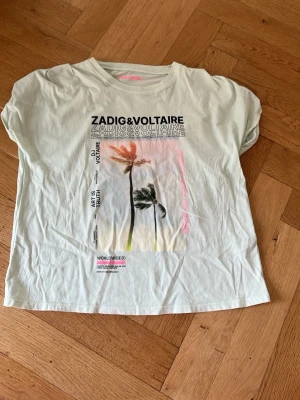 Turkos Zadig & Voltaire t-shirt med tryck - Cool turkos t-shirt från Zadig & Voltaire med tryck av palmer och text framtill. T-shirten har korta ärmar och en avslappnad passform. Perfekt för en trendig och avslappnad stil.