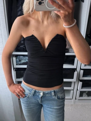 Svart axelbandslös tubtopp  - Snygg svart axelbandslös tubtopp / bandeau med djup v-ringning och figurnära passform. Från bikbok strl xs men passar mig med s då den är stretchig 