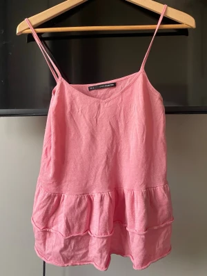 Rosa volang-linnetopp  - Söt rosa linnetopp med tunna axelband och volangdetaljer nertill. Toppen har en avslappnad passform och är perfekt till sommaren. Köpt för ett år sedan och har använts bara några gånger❣️