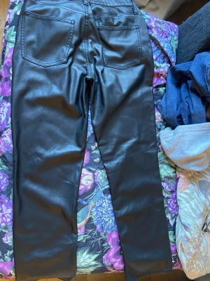 Svarta fuskskinnbyxor med raka ben - Säljer ett par svarta byxor i fuskskinn med raka ben och hög midja. Byxorna har två bakfickor och bälteshällor. Snyggt glansigt material som ger en cool look. Perfekta att styla med en oversized tröja eller crop top.
