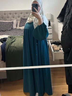 Teal maxiklänning med vida ärmar - Säljer en petrolblå maxiklänning med långa, vida ärmar och rund halsringning. Klänningen har en lös och flowy passform som ger en snygg siluett. Perfekt för dig som gillar modest mode och vill ha något bekvämt och stilrent.