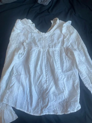 Vit blus med volang från Stradivarius - Söt vit blus från Stradivarius med volangdetaljer vid axlarna och strukturmönster i tyget. Blusen har rundad halsringning och långa ärmar med resår vid ärmsluten. Perfekt för en trendig och feminin look. Kontakta gärna ❤️