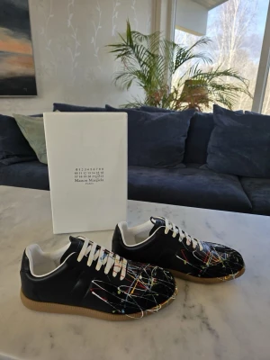 Maison margiela skor (svarta) - Hej! Jag säljer dessa skor då dem inte är i min storlek. Dem är svarta med snyggt färg skvätt på. Dem är knappast använda, du får med box och jag har kvitto på dem. Hör av er vid minsta fundering!