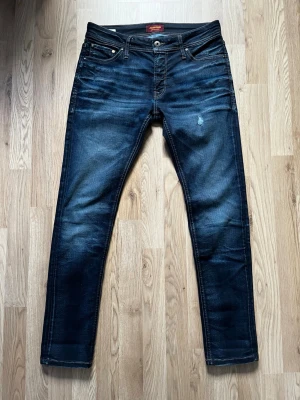 Mörkblå slim fit jeans från Jack & Jones - Snygga mörkblå slim fit jeans från Jack & Jones med klassisk femficksdesign och diskreta slitningar framtill. Jeansen har en något tvättad look och raka ben. Perfekta för en trendig och avslappnad stil.