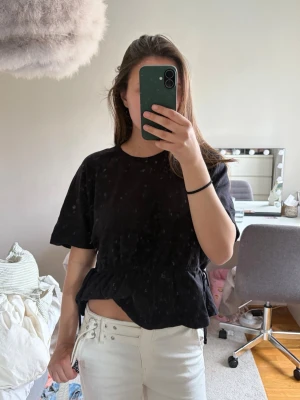 Svart topp med resår i midjan - Svart topp med korta ärmar och rund halsringning. Toppen har knytning i midjan!