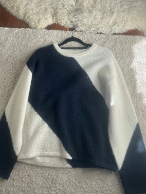 Stickad tröja från Gina Tricot - Säljer en mysig stickad tröja från Gina Tricot med stora diagonala block i svart och vitt. Tröjan har rund halsringning och långa ärmar. Perfekt för dig som gillar en enkel men ändå cool look.