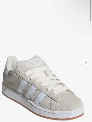 Beige Adidas Campus sneakers - Säljer ett par beige Adidas Campus sneakers med klassiska vita ränder på sidan och vit logga på tungan. Skorna har en låg profil och är tillverkade i mocka med gummisula. Perfekt för dig som gillar stilrena och tidlösa sneakers.Säljer dessa skor då jag har köpt nya. Köpte dessa i november alltså är de ganska hyfsat nya, har inte hunnit använda dem mycket då det har varit vinter. Dock har de blivit lite blåa på grund av mina byxor, men annars ser de inte så använda ut. Kan tänka mig sänka priset🤍