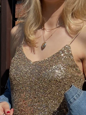 Glittrig guldig linnetopp  (slutsåld online) - Säljer mitt fina glittriga  linne i guld med tunna axelband och v-ringad . Axelbandet går att justera så att v-ringningen passar ens byst! Den är från Esprit så bra kvalitet! 