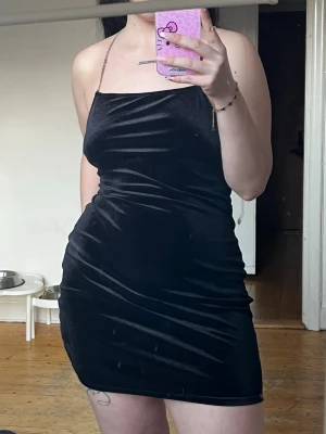 Svart sammetsklänning med strassband - Supersnygg svart kort klänning i sammet med tunna axelband täckta av strass. Figurnära passform och enkel, stilren design som ger en lyxig känsla. Perfekt för dig som vill sticka ut lite extra.