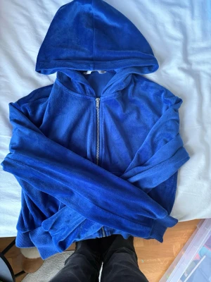 Blå zip-hoodie från H&M - Mysig blå hoodie från H&M i mjukt velourmaterial. Tröjan har dragkedja framtill, huva och långa ärmar med muddar. Perfekt för en chill och avslappnad stil.