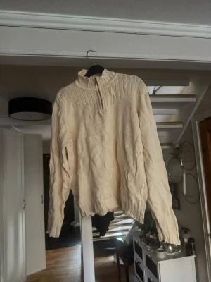 stickad tröja med halv dragkedja - Mysig beige stickad tröja med halv dragkedja i halsen och ribbstickade detaljer upptill. Tröjan har lång ärm och avslappnad passform, perfekt för lager på lager. Passar dig som gillar enkel och stilren design.